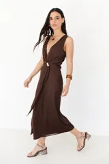 Vestido midi marrón con escote en V, sin mangas y detalle de nudo con aro dorado en la cintura.