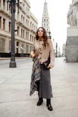 Falda midi de diseño asimétrico que combina paño gris liso con un panel lateral de tela escocesa en tonos grises, marrones y blancos. Presenta un corte irregular con bordes desflecados y tajos laterales.