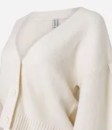 Cardigan de punto color crema con escote en V, cierre frontal de botones y mangas largas abullonadas con puños acanalados. Presenta un diseño corto y ajuste cómodo.