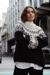 Sweater de lana con diseño de jacquard en la parte superior, cuello redondo, mangas largas y puños acanalados. Presenta un corte holgado con tajos laterales y un diseño ligeramente más corto en la parte delantera.