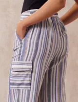 Pantalón de lino con rayas verticales en tonos beige, azul y gris. Tiene pretina elastizada, bolsillos inclinados en la parte delantera y un bolsillo tipo cargo en el lateral. Marca Zac & Rachel.