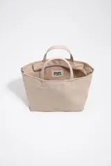 Bolso shopper mediano de mano Bimba y Lola color marrón, confeccionado en poliamida con detalles en cuero y herrajes metálicos dorados. Cuenta con doble asa de mano, correa de hombro ajustable de lona beige, cierre superior con cremallera y logo impreso en dorado al frente.