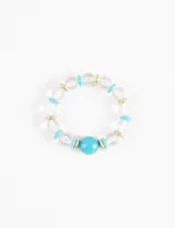 Pulsera elástica con cuentas de vidrio transparentes, cuentas cilíndricas turquesas y detalles dorados.
