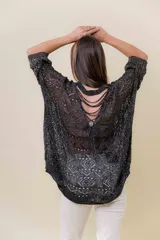 Buzo de tejido liviano y calado con brillo sutil, color gris oscuro o negro. Presenta un calce amplio y mangas amplias, con un detalle de tiras entrelazadas en la espalda. El largo es irregular, más largo en la parte trasera.