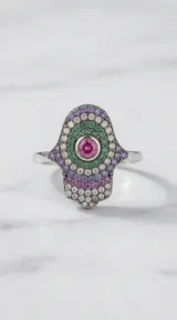 Anillo de plata 925 con diseño de mano de Hamsa, decorado con circonias en tonos verde, violeta y blanco, y una piedra central rosada.
