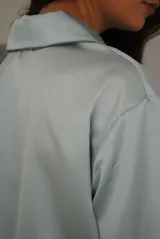 Pijama de satén elastizado color celeste, compuesto por una camisa de manga larga con cuello solapa, botones frontales y bolsillo en el pecho, y un pantalón recto con cintura elástica y lazo ajustable.