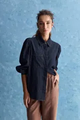 Camisa de jean azul oscuro con calce relajado, cuello clásico, bolsillo aplicado en el delantero y mangas largas abullonadas con puños abotonados.