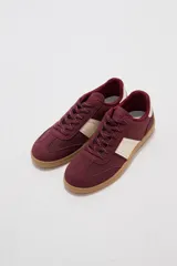 Zapatillas bordó de estilo urbano, con detalles en beige en los laterales, cordones estampados y suela de goma marrón.