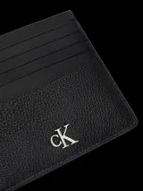 Tarjetero de cuero negro granulado con múltiples ranuras para tarjetas y el logo 'CK' metálico en la parte frontal.