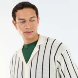 Camisa de manga corta de punto calado en color beige con rayas verticales negras, cuello tipo polo y cierre frontal con botones.