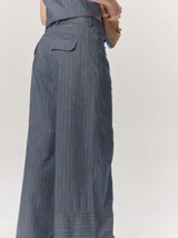 Pantalón sastrero de corte ancho, color beige con rayas verticales blancas y detalles de costuras pespunteadas.