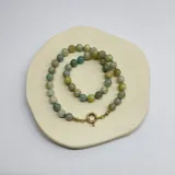 Collar compuesto por cuentas esféricas de piedra natural amazonita de 8 mm, unidas mediante nudos de hilo color turquesa. Presenta un cierre frontal tipo mosquetón circular con baño de oro.