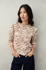 Blusa color crema con estampado animal print de cebra en marrón, corte relajado, mangas 3/4 fruncidas y cuello con volados.