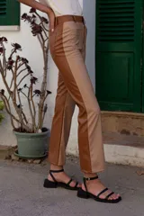 Pantalón de cuero sintético color marrón claro y marrón oscuro, de tiro medio/alto y silueta levemente acampanada desde la rodilla. Tiene bolsillos cuadrados y combina dos colores en frente y espalda.