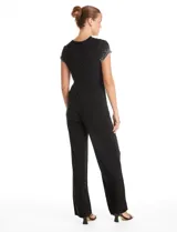 Enterito de seda fría color negro, con escote en V cruzado, mangas cortas decoradas con apliques de brillo y perlas, cintura elástica con lazo lateral ajustable y pierna de corte recto.