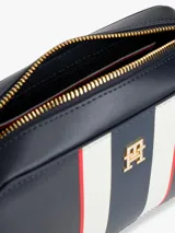 Cartera tipo bandolera de Tommy Hilfiger, confeccionada en poliuretano color azul marino. Presenta un diseño rectangular con una franja vertical central en colores blanco, azul y rojo, y el logo monograma TH en metal dorado en el frente. Incluye correa ajustable y cierre superior.