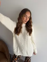 Buzo de punto en color beige, con diseño de trenzas verticales en el frente, cuello redondo y mangas largas con puños acanalados.