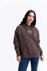 Buzo tipo canguro color marrón chocolate, con capucha ajustable mediante cordones, bolsillo frontal tipo canguro y parche rectangular con logo de la marca Mistral en el pecho.