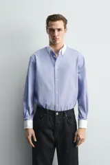 Camisa de corte regular fit confeccionada en tejido ligero de algodón, con diseño de rayas verticales azules y blancas. Presenta cuello abotonado y puños en color blanco a contraste, con cierre frontal de botones.