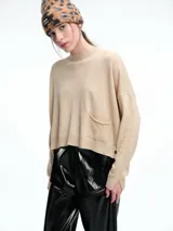 Sweater de tejido de punto color beige, con cuello redondo, hombros caídos y costura central vertical en el frente. Presenta un diseño de corte relajado, con largo asimétrico y aberturas laterales en el ruedo.