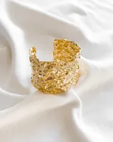 Brazalete rígido dorado con textura irregular.