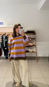 Buzo de tejido de punto con diseño a rayas horizontales en tonos lila y mostaza. Presenta cuello redondo, mangas largas con puños ajustados en color marrón y ruedo recto en el mismo tono. Incluye un pequeño detalle bordado en el pecho.