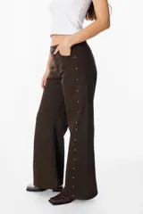 Jean de corte recto y tiro medio, color azul, con detalles de tachas metálicas doradas a lo largo de las costuras laterales externas.