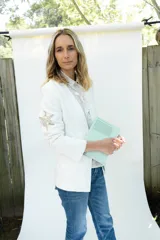 Blazer de lino blanco con solapa clásica, cierre de un botón frontal y detalle de bordado dorado en la manga.
