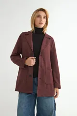 Chaqueta de gamuza sintética color bordó, con cuello solapa, cierre frontal de botones y cinturón ajustable del mismo material. Posee bolsillos frontales y mangas largas.