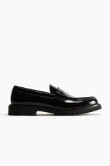 Mocasines de cuero sintético negro con suela gruesa track, costuras prominentes en la puntera y detalle de antifaz en el empeine.