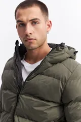 Campera puffer con capucha, diseño acolchado, cierre frontal y bolsillos laterales. Presenta un interior en contraste de color verde oliva.