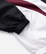 Campera con capucha de estilo deportivo, confeccionada en poliéster con diseño de paneles en colores negro, blanco y bordó. Presenta cierre frontal con cremallera, puños elásticos y bolsillos laterales.