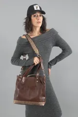 Bolso marrón de cuero vacuno liso con detalles en cuero grabado símil reptil. Tiene estructura definida, forro interior de tela con bolsillos y divisiones, bolsillo trasero con cierre, dos asas cortas y una correa larga extensible y desmontable trenzada con tientos.