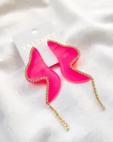 Par de aros colgantes de acrílico fucsia con forma de ala y borde con strass dorados.