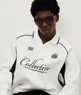 Buzo deportivo de felpa en color blanco con detalles en negro. Presenta cuello tipo polo, mangas largas con puños acanalados y diseño con recortes laterales. Incluye estampados gráficos en el frente con tipografía cursiva y emblema circular.