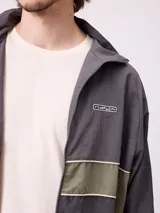 Rompevientos Rusty con cierre frontal, capucha y diseño de bloques de color en gris y verde militar. Cuenta con puños elásticos y logo de la marca en el pecho.