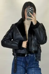 Campera tipo aviador de cuero sintético negro con interior y detalles de piel sintética al tono en cuello, puños y ruedo. Presenta cierre frontal cruzado y cinturón ajustable con hebilla metálica en la cintura.