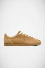 Zapatillas planas de gamuza en color tostado, con diseño minimalista, suela de goma al tono y cordones blancos.