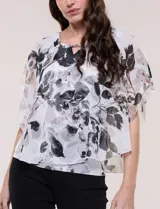 Blusa de gasa semitransparente con hilos de lúrex, diseño estampado floral en tonos blanco, gris y negro, silueta holgada tipo capa y escote redondo con detalle metálico.