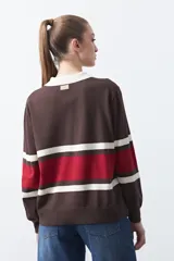Sweater de tejido de punto con diseño a rayas horizontales en tonos marrón, rojo y crema. Presenta cuello tipo polo con cierre frontal de botones y mangas largas con puños ajustados.