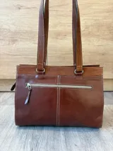 Cartera de cuero marrón de tamaño medio con diseño estructurado, que combina cuero liso y un panel frontal texturizado tipo cocodrilo con bolsillo exterior con cierre. Cuenta con doble asa de hombro y costuras visibles de contraste.