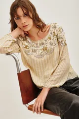 Camisa de tul color beige con bordados florales en el escote y mangas largas. Presenta detalles de lentejuelas y canutillos dorados y plateados en todo el diseño, con un patrón de rayas verticales en el cuerpo y mangas.