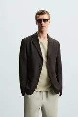 Blazer regular fit color marrón oscuro confeccionado en tejido de lino. Tiene cuello con solapas de muesca, manga larga con puño abotonado, bolsillo de vivo en el pecho, bolsillos de solapa en la cadera, bolsillo interior, bajo con aberturas en la espalda y cierre frontal con botonadura.