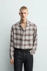 Camisa relaxed fit de manga larga con cuello solapa, confeccionada en tejido con mezcla de viscosa. Presenta un bolsillo plastrón en el pecho, bajo con aberturas laterales y cierre frontal de botonadura. El diseño es a cuadros en tonos beige y marrón.