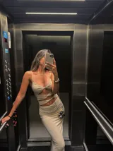 Vestido largo color beige con escote halter, corte ajustado y aberturas en la zona del abdomen.