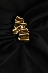 Top de punto fino color negro, con diseño de un solo hombro y escote asimétrico. Presenta un panel fruncido en el hombro con un adorno metálico dorado y drapeado lateral en la cintura que aporta un efecto entallado.