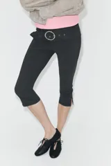 Pantalón capri de tiro medio confeccionado en tejido elástico, con cintura elástica y detalle de cinturón integrado con hebilla metálica circular. Presenta aberturas en el bajo.