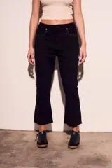 Pantalón de jean negro con corte flare, tiro medio y detalles de tachas plateadas en los bolsillos delanteros.