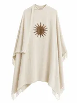 Ruana de lana color beige con textura de espiga, terminaciones con flecos y aplique bordado de sol en el centro.