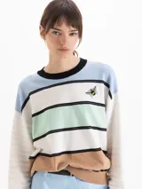 Sweater Clover de tejido semi liviano, de calce oversize con escote redondo, hombros caídos y mangas largas. Su diseño a rayas horizontales combina celeste, blanco, verde menta, negro y marrón, e incluye un bordado de abeja en el frente.